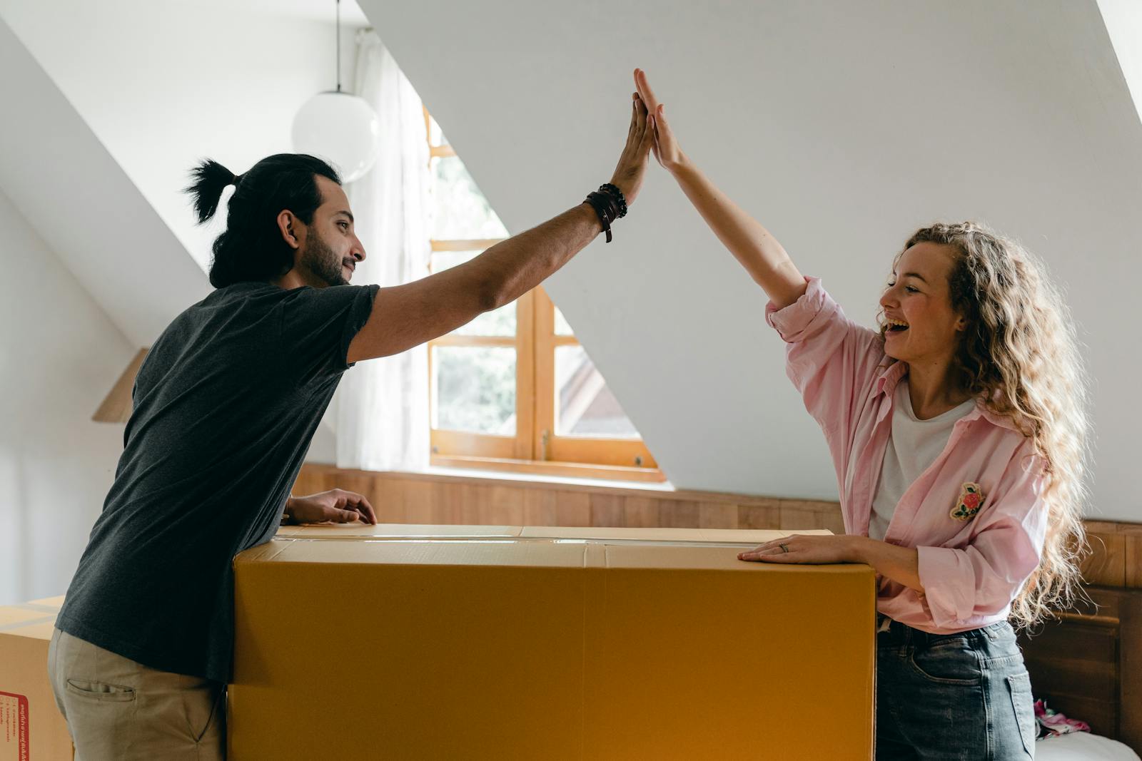 renters Young couple high-fiving in their new home, happily surrounded by moving boxes.