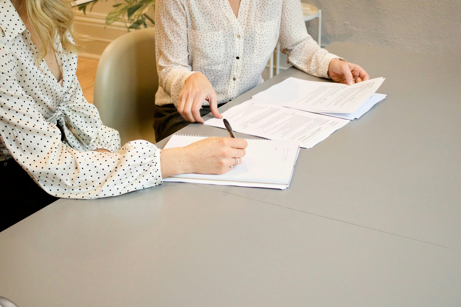 woman signing on white printer paper beside woman about to touch the documents bonds